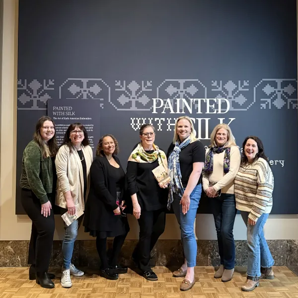 A group of seven people stand in front of the entrance to the exhibition "Painted with Silk"